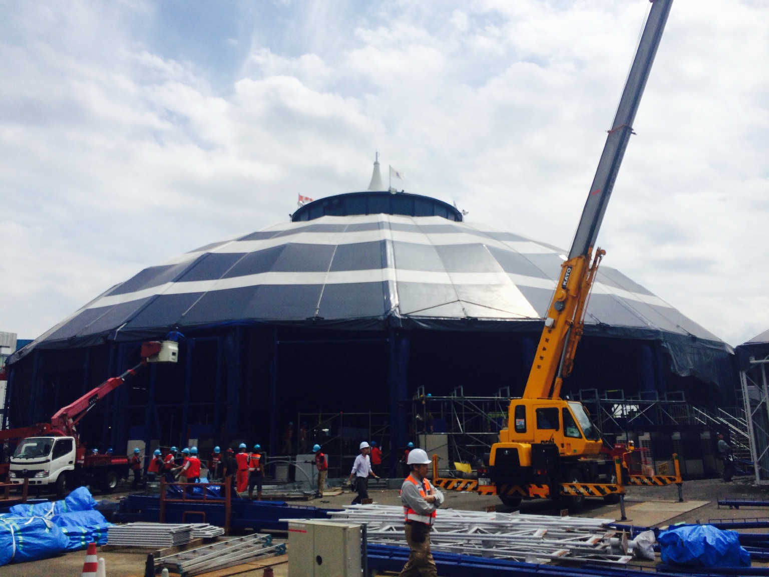 A crane, work platforms and crews outside a large touring tent