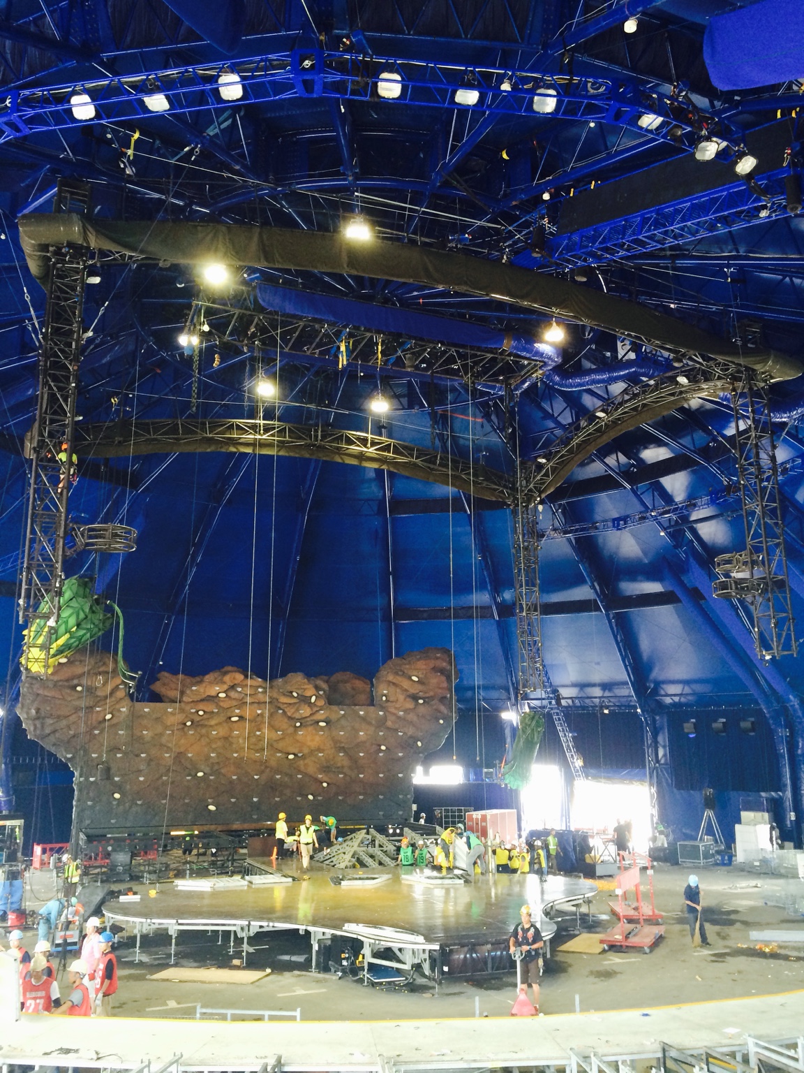 Overhead rigging and crews assembling a stage inside a blue big top