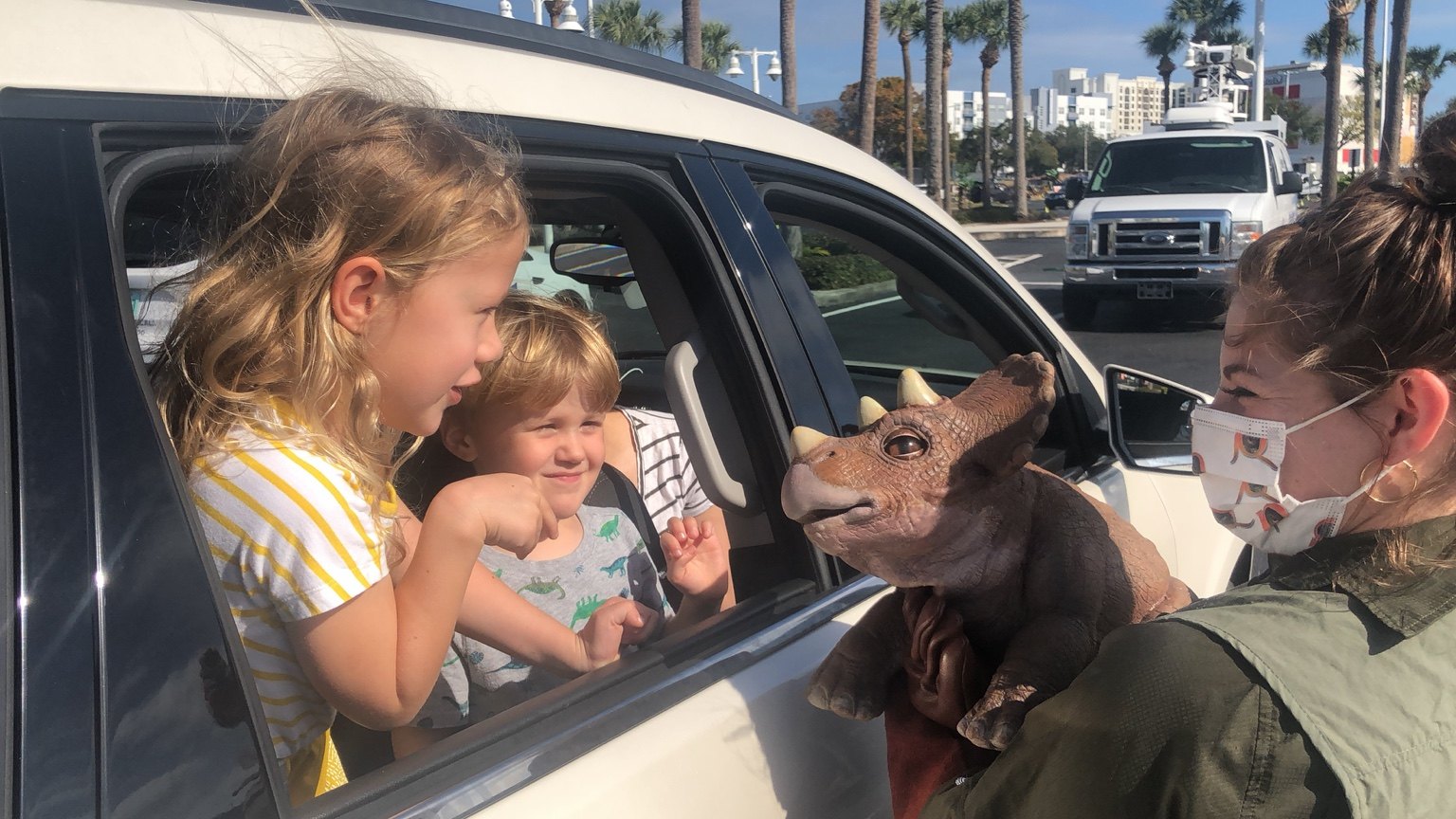 Children meet a baby dinosaur puppet from their car during the Jurassic Quest drive-through